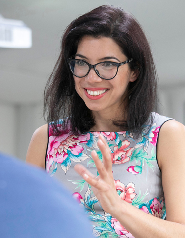 daniela-bultoc-speaking-higher-education-consultant.png Daniela Bultoc speaking with enthusiasm during a professional discussion, wearing a floral dress and smiling while gesturing with her hand.